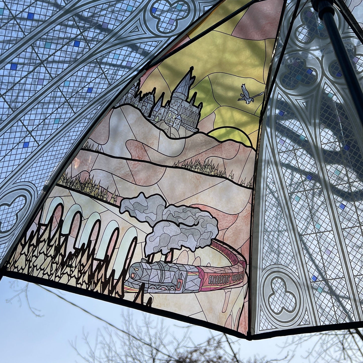 Wizard-inspired stained glass canopy umbrella featuring illustrated panels of a magical castle, whimsical crooked house, enchanted willow tree, grand candlelit dining hall, and vintage steam train.